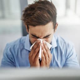 Shot of a young businessman blowing his nose with a tissue at work