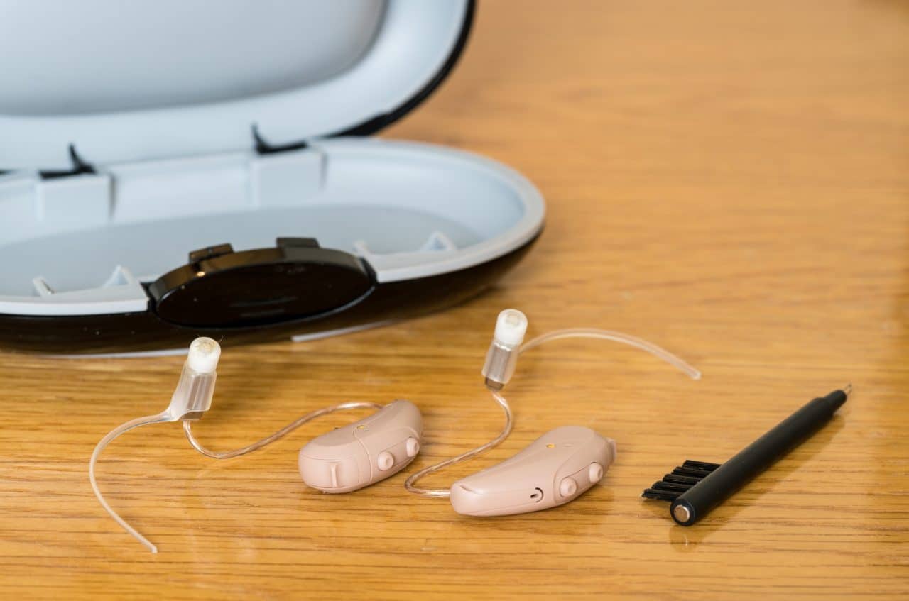 Close up of hearing aids, cleaning brush and storage case.