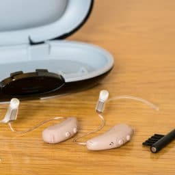 Close up of hearing aids, cleaning brush and storage case.