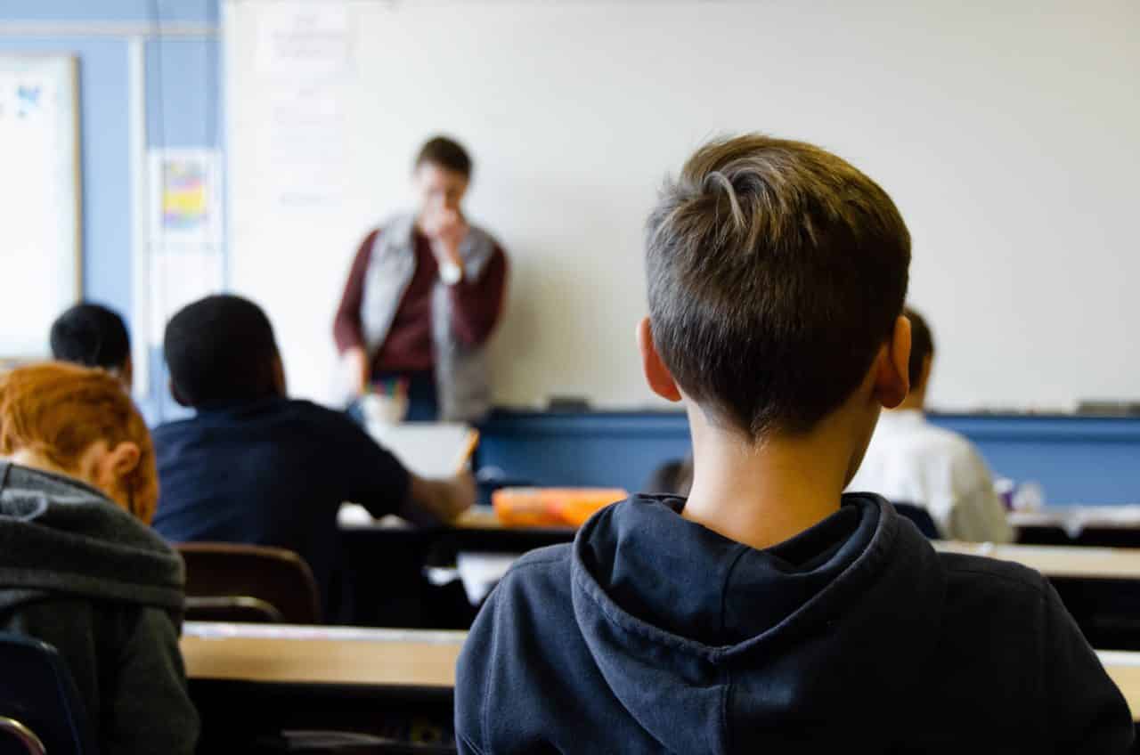 Students listening to a teacher in a classroom setting.