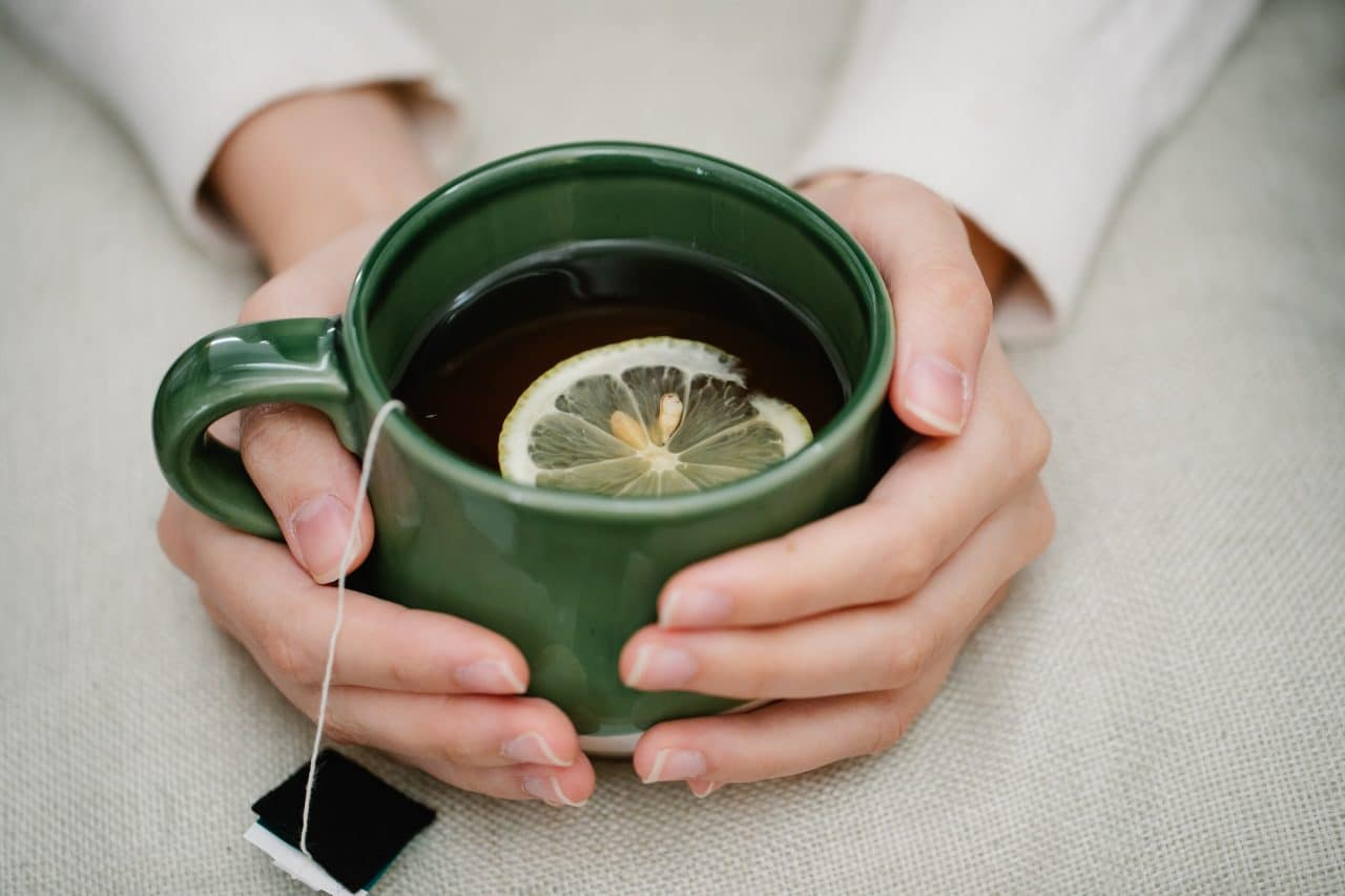 Woman's hands wrapped around a mug of hot tea with lemon.