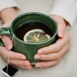 Woman's hands wrapped around a mug of hot tea with lemon.