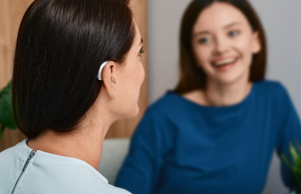 Woman with hearing aids chatting with her friend indoors.