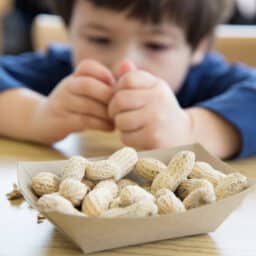 Little boy sitting in front of a container of peanuts.