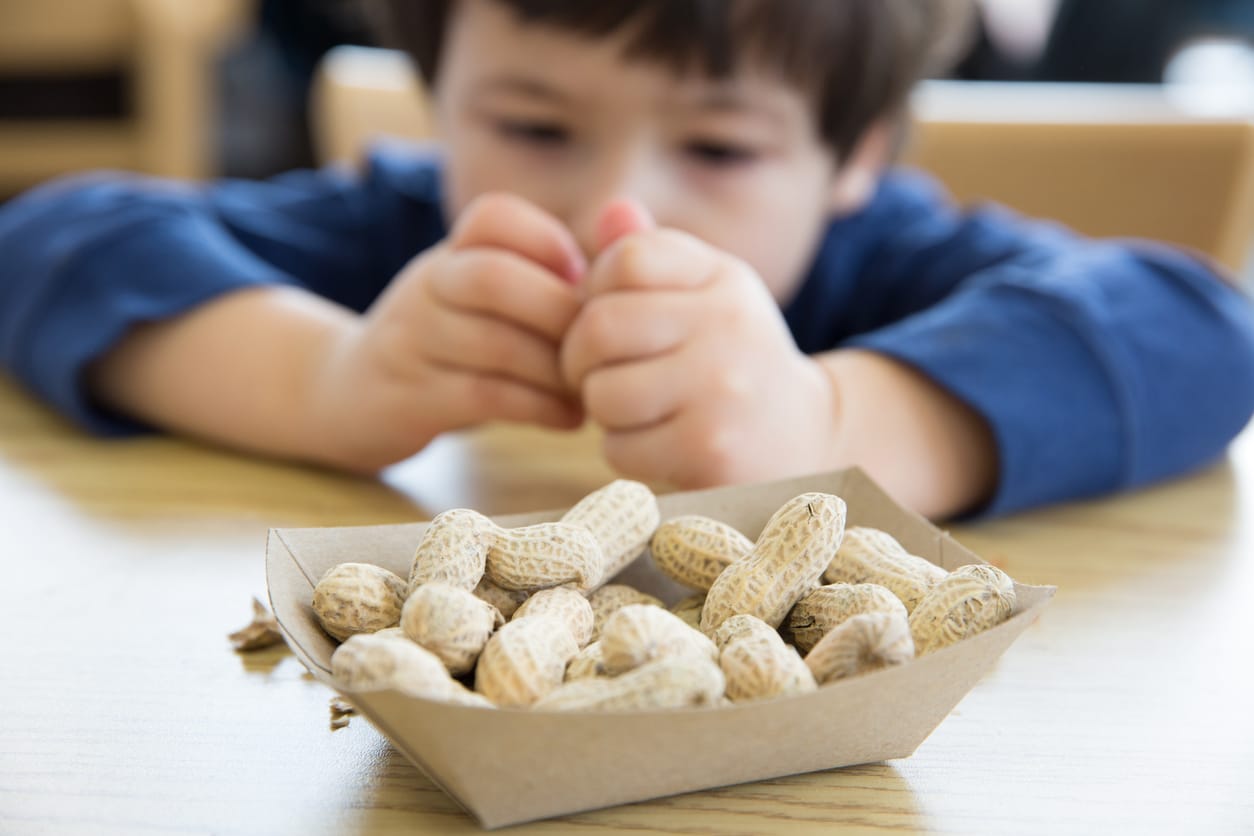 Little boy sitting in front of a container of peanuts.