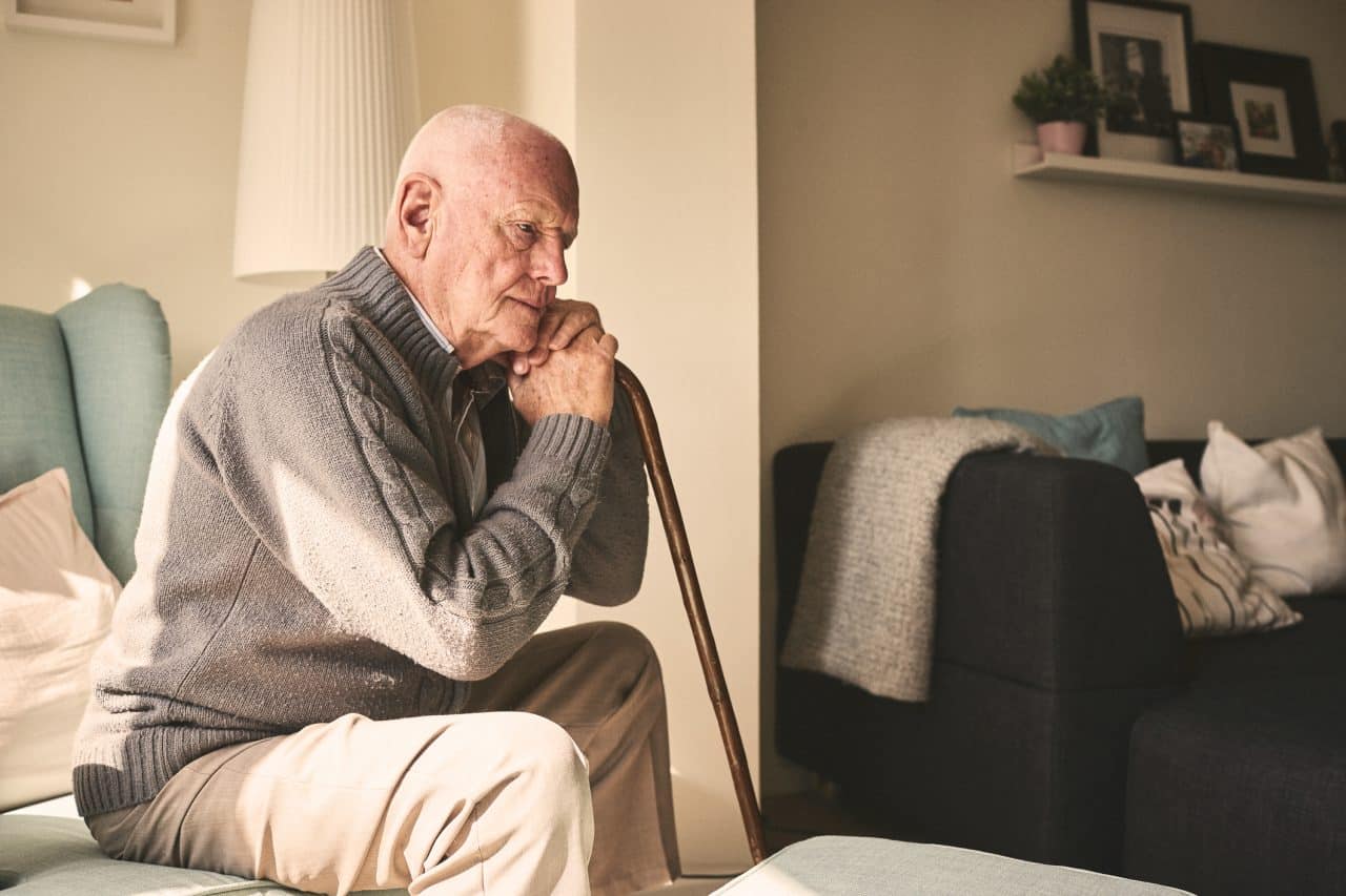 A thoughtful looking senior man sitting alone on his bed.