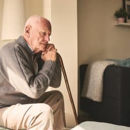 A thoughtful looking senior man sitting alone on his bed.