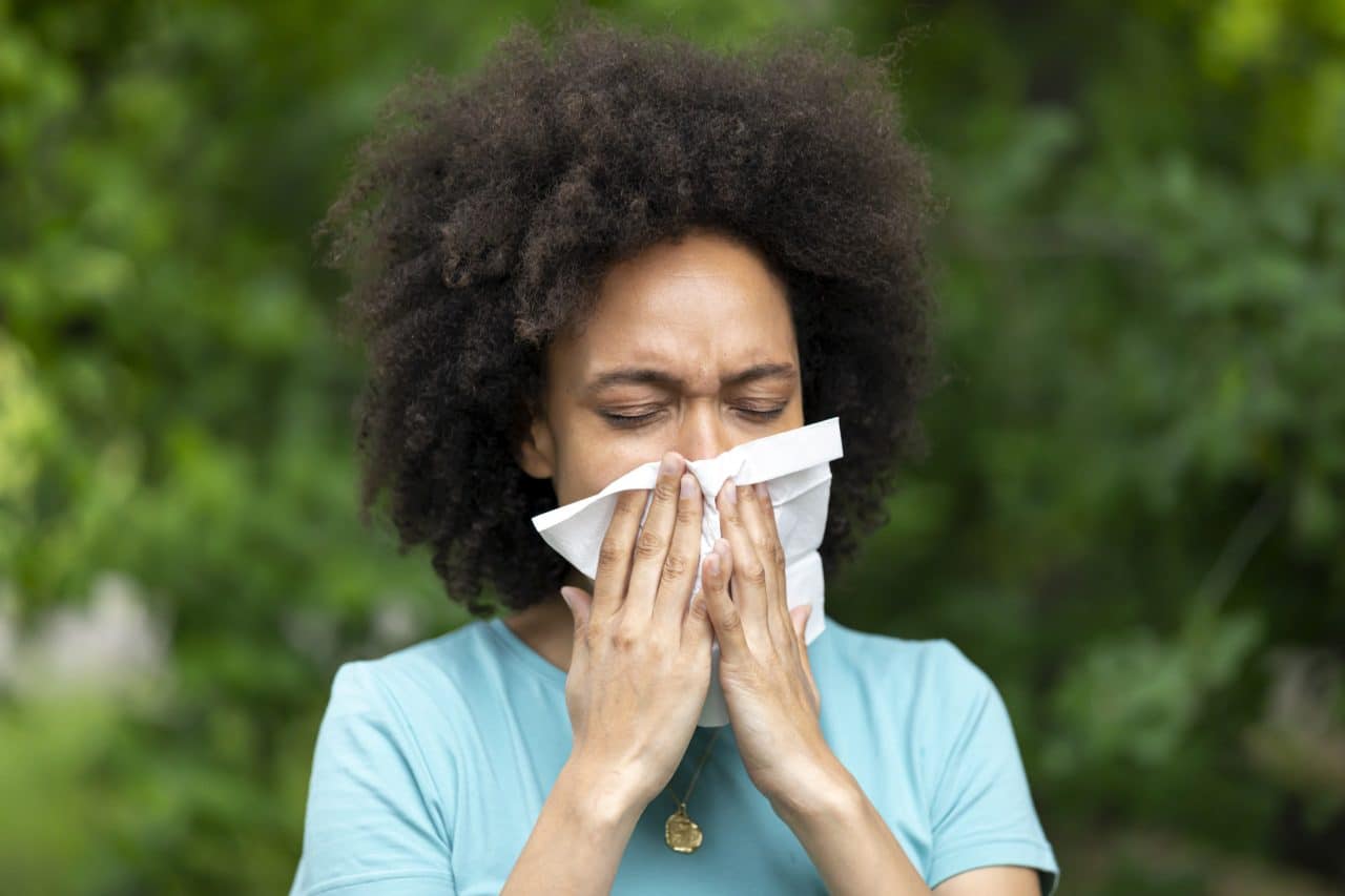 Woman experiencing allergies or sinus pressure blowing her nose with a tissue.