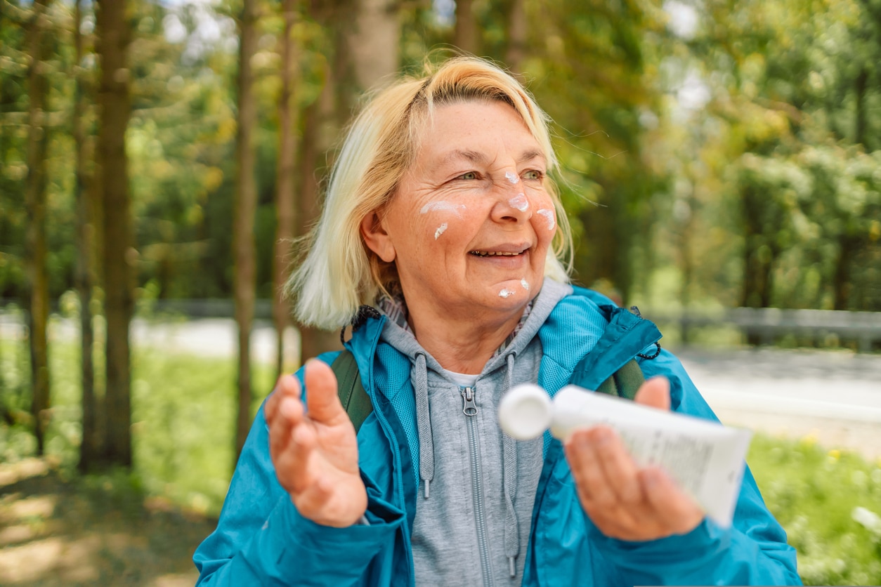 Woman applying sunscreen on her face while walking in the woods