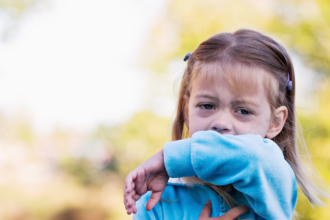 Little girl with allergies sneezing into her elbow.