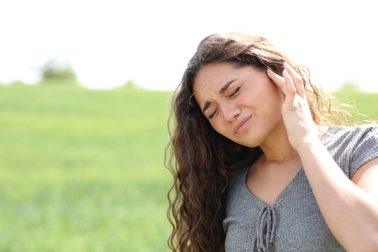 Woman in field with tinnitus holds ear