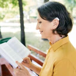 Woman with hearing aids reading a book in the park