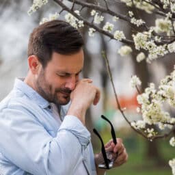 Man with pollen allergies rubbing his nose next to a flower tree