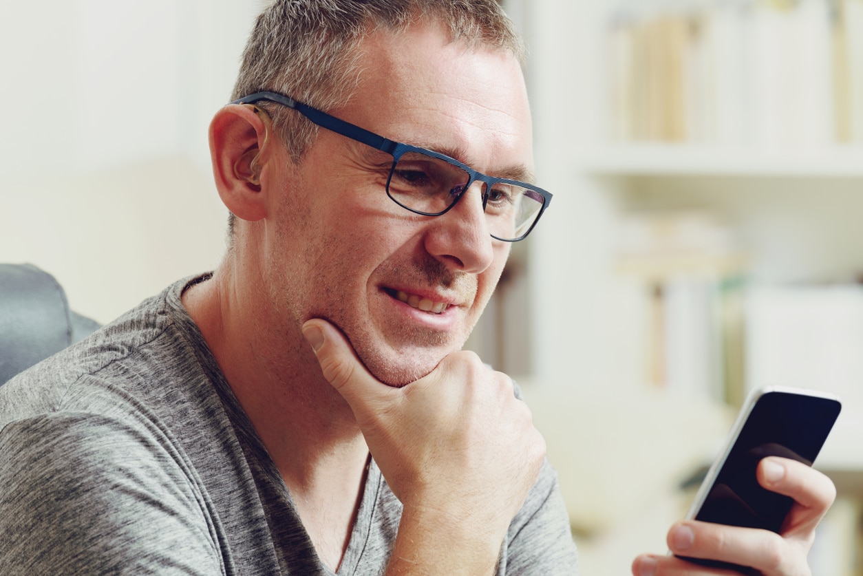 Man with hearing aid looks at phone