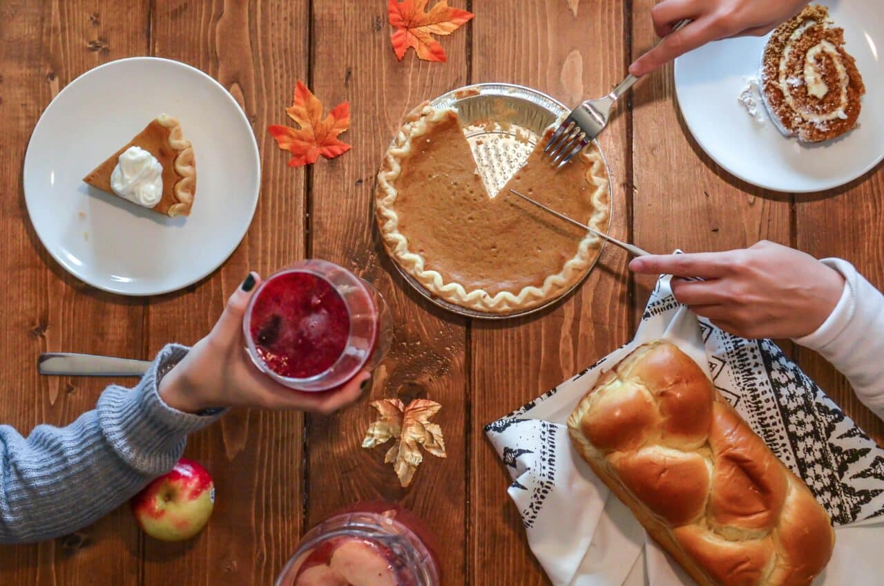 Hands above a Thanksgiving dinner table with pumpkin pie and challah bread