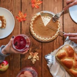 Hands above a Thanksgiving dinner table with pumpkin pie and challah bread